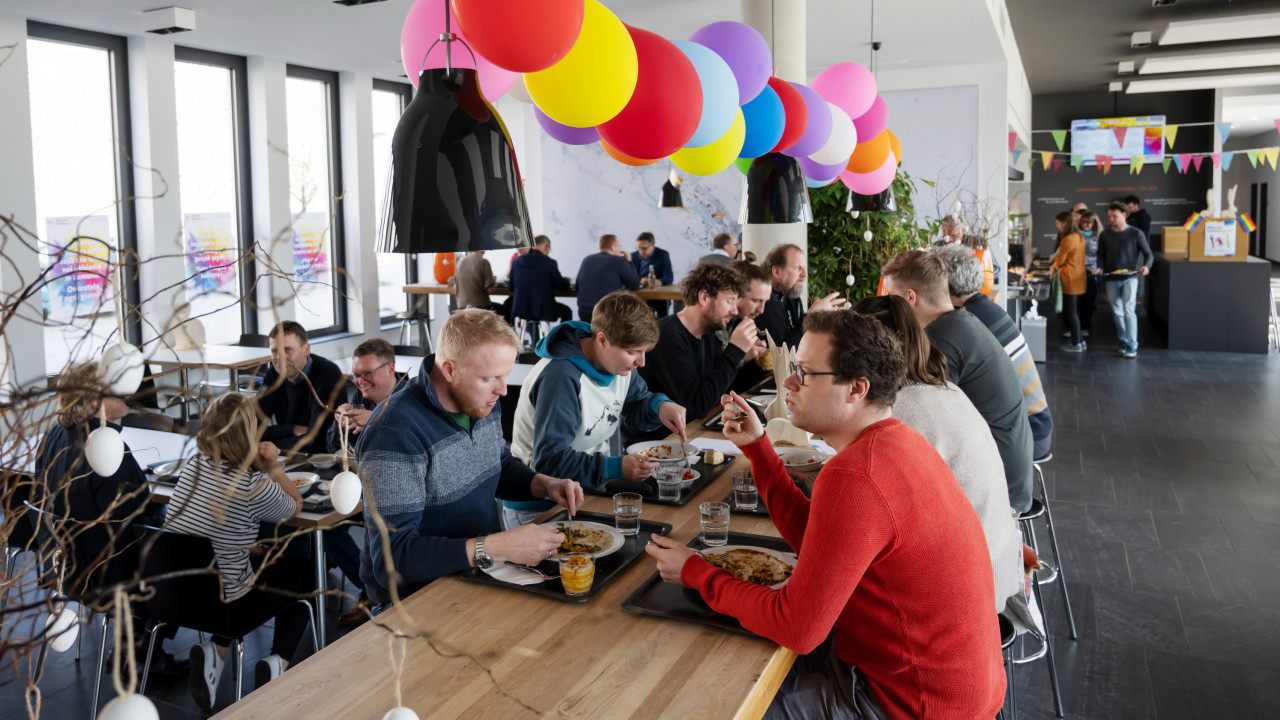 Blick in die bunt dekorierte hanseWasser-Kantine, im Vordergrund eine großer langer Tische, an dem die Kolleg*innen zu Mittag essen