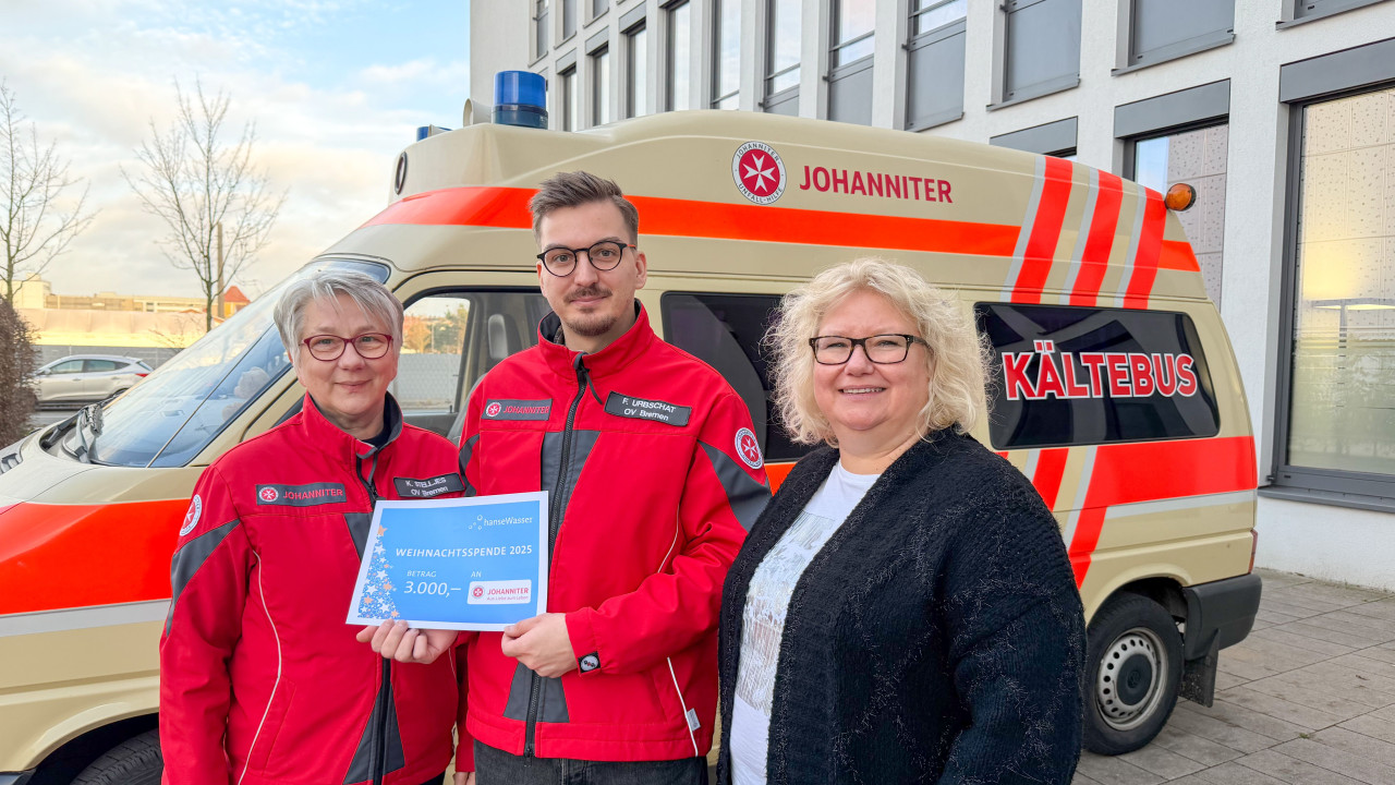 Drei Personen stehen vor dem historischen Kältebus der Johanniter. Eine Person hat den Spendenscheck in der Hand.