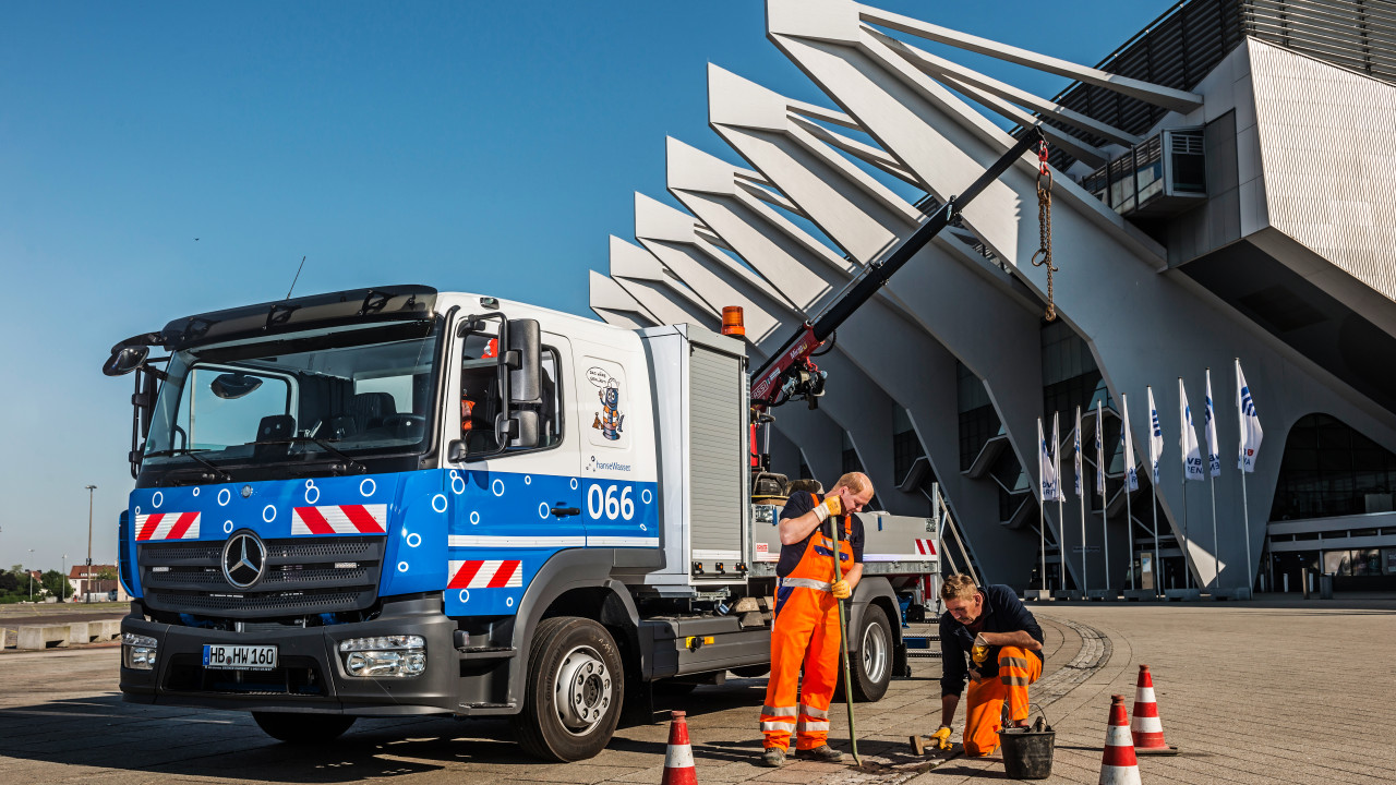 Ein Wagen der hanseWasser parkt vor der ÖVB-Arena, zwei Mitarbeiter*innen untersuchen einen Kanaldeckel